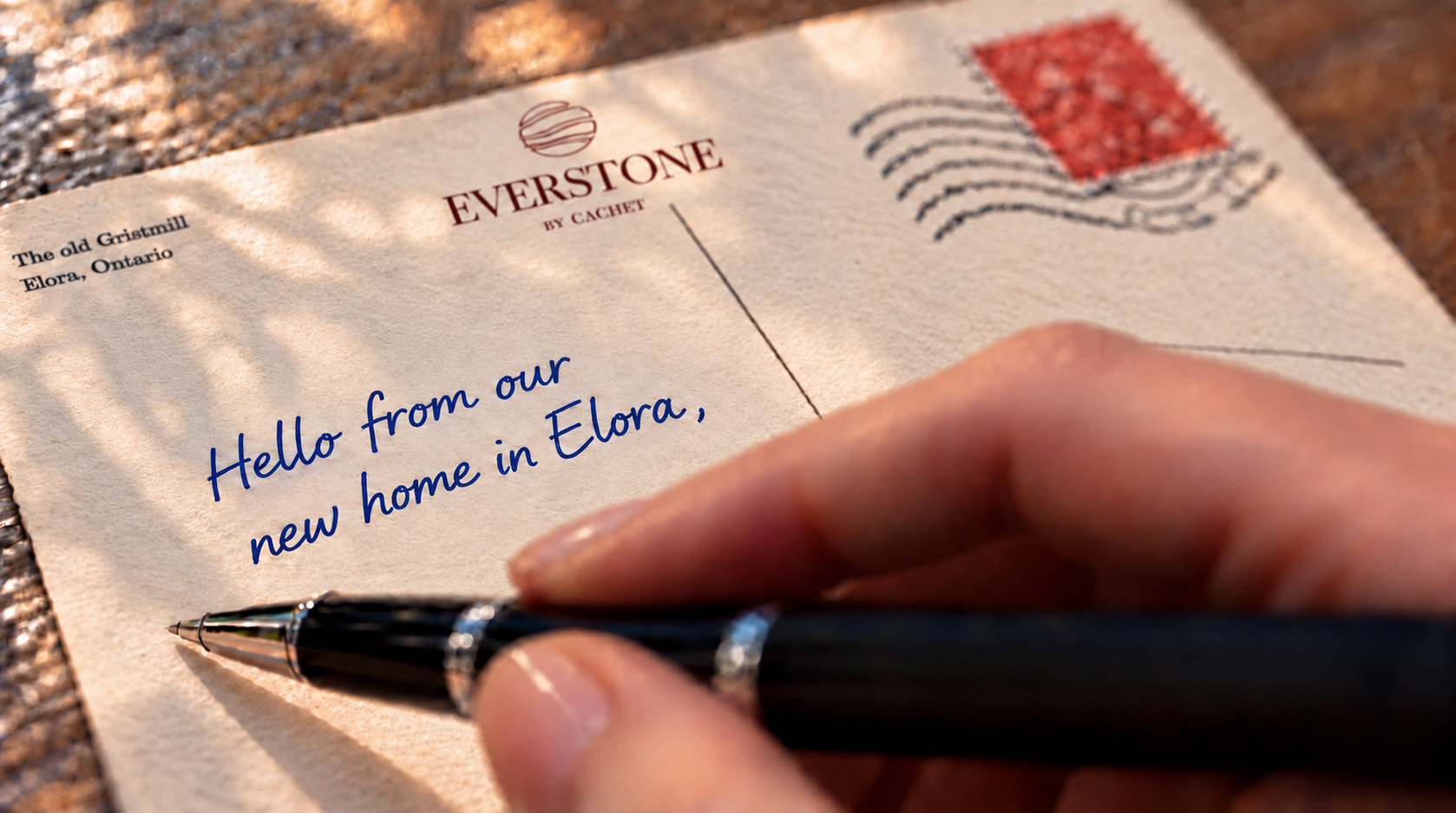 Everstone branded postcard with a partially written message and a hand positioned to continue writing